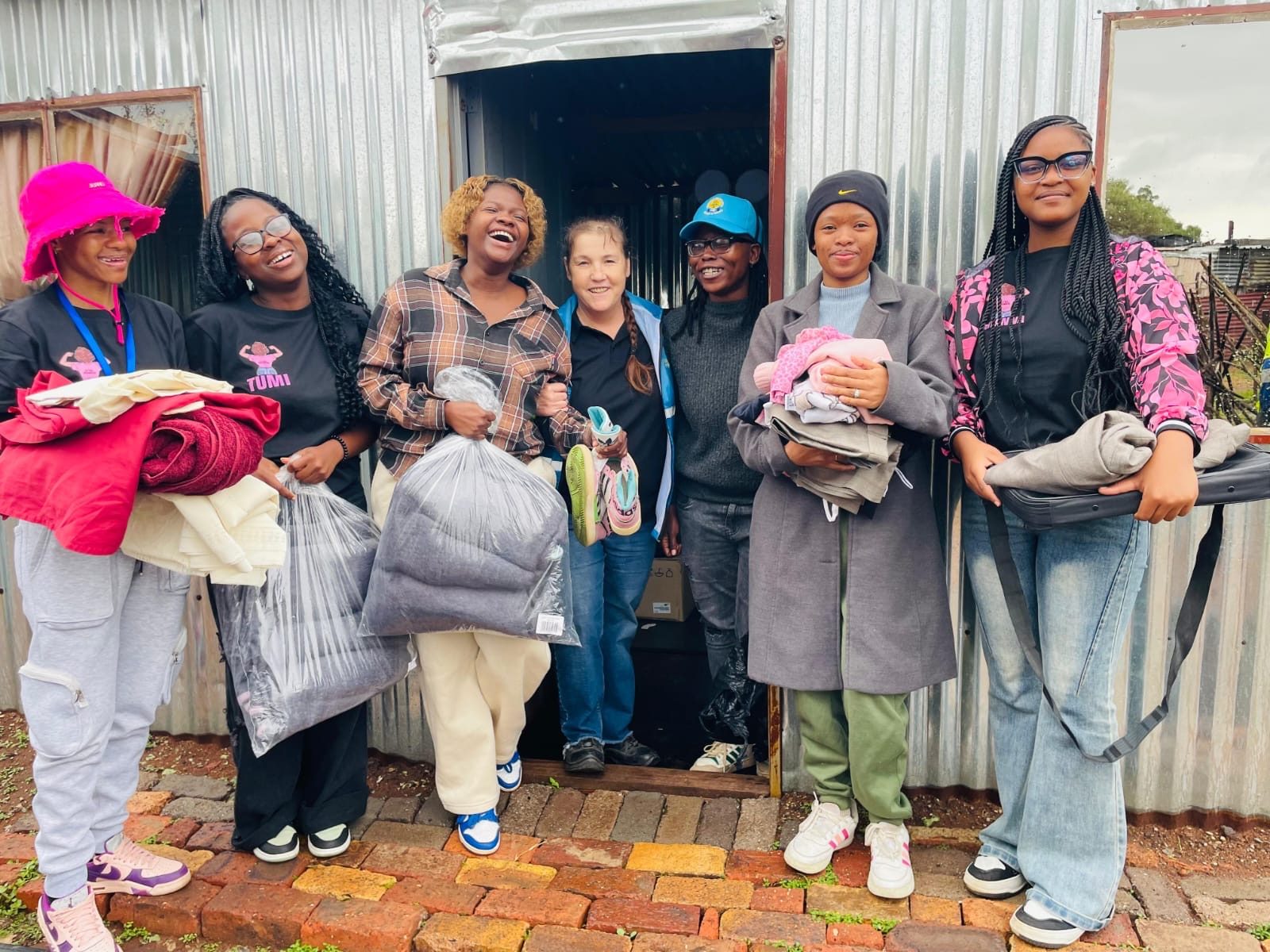 Team of volunteers holding bags of donated clothing outside a community home